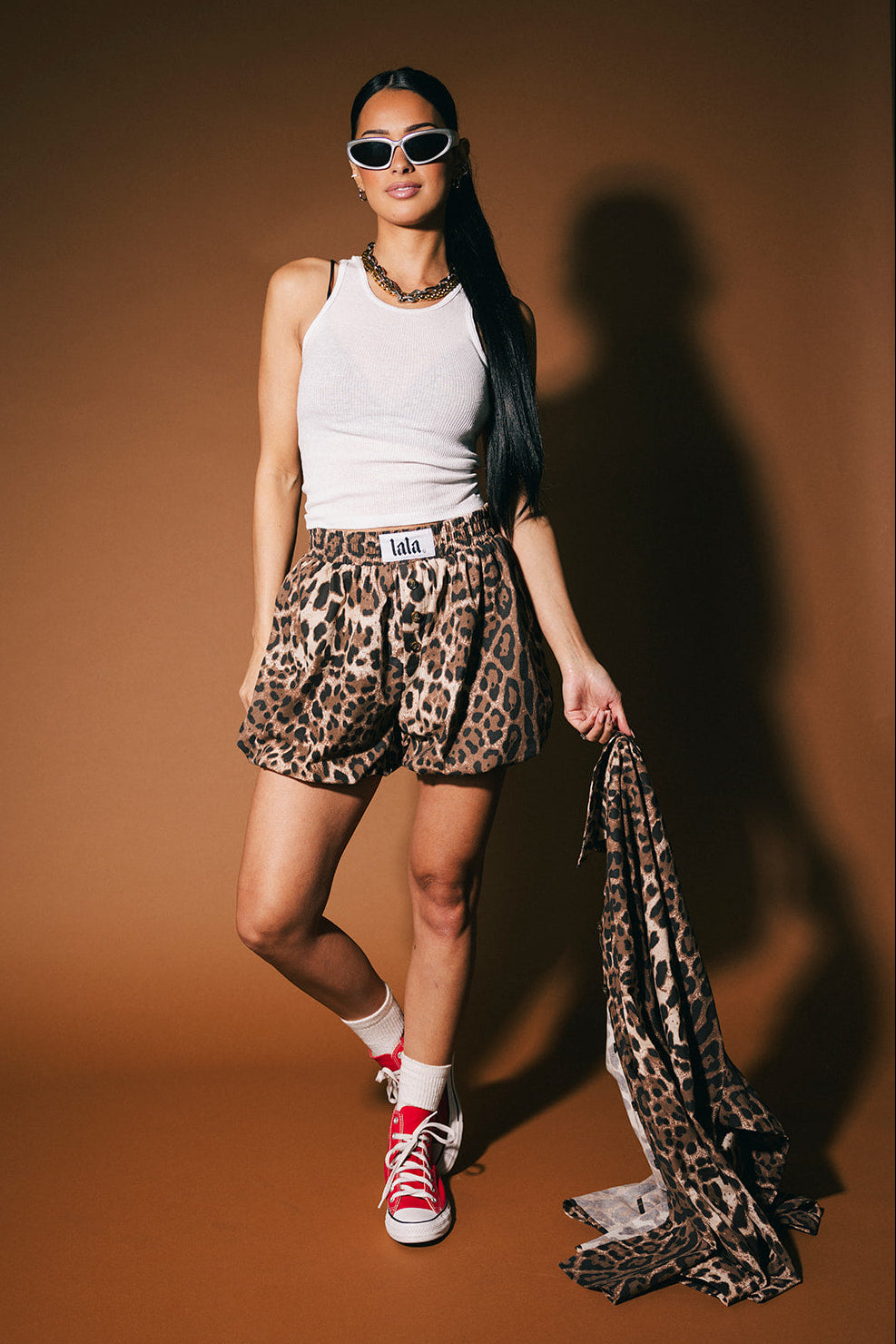 Woman wearing leopard print shorts and a white tank top against a brown background