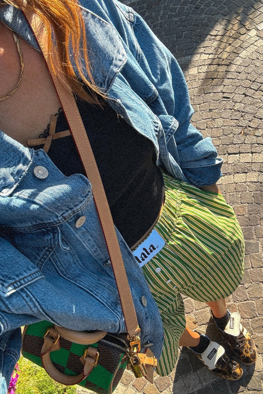 photo of girl wearing green and yellow stripe boxer shorts with elastic waistband that has a white "lala" label at the front, 3 button faux fly, and side pockets