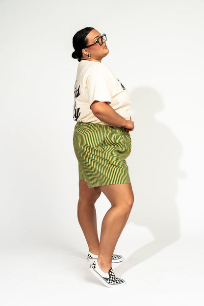 photo of girl wearing green and yellow stripe boxer shorts with elastic waistband that has a white "lala" label at the front, 3 button faux fly, and side pockets