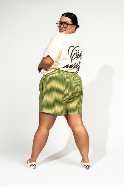 photo of girl wearing green and yellow stripe boxer shorts with elastic waistband that has a white "lala" label at the front, 3 button faux fly, and side pockets