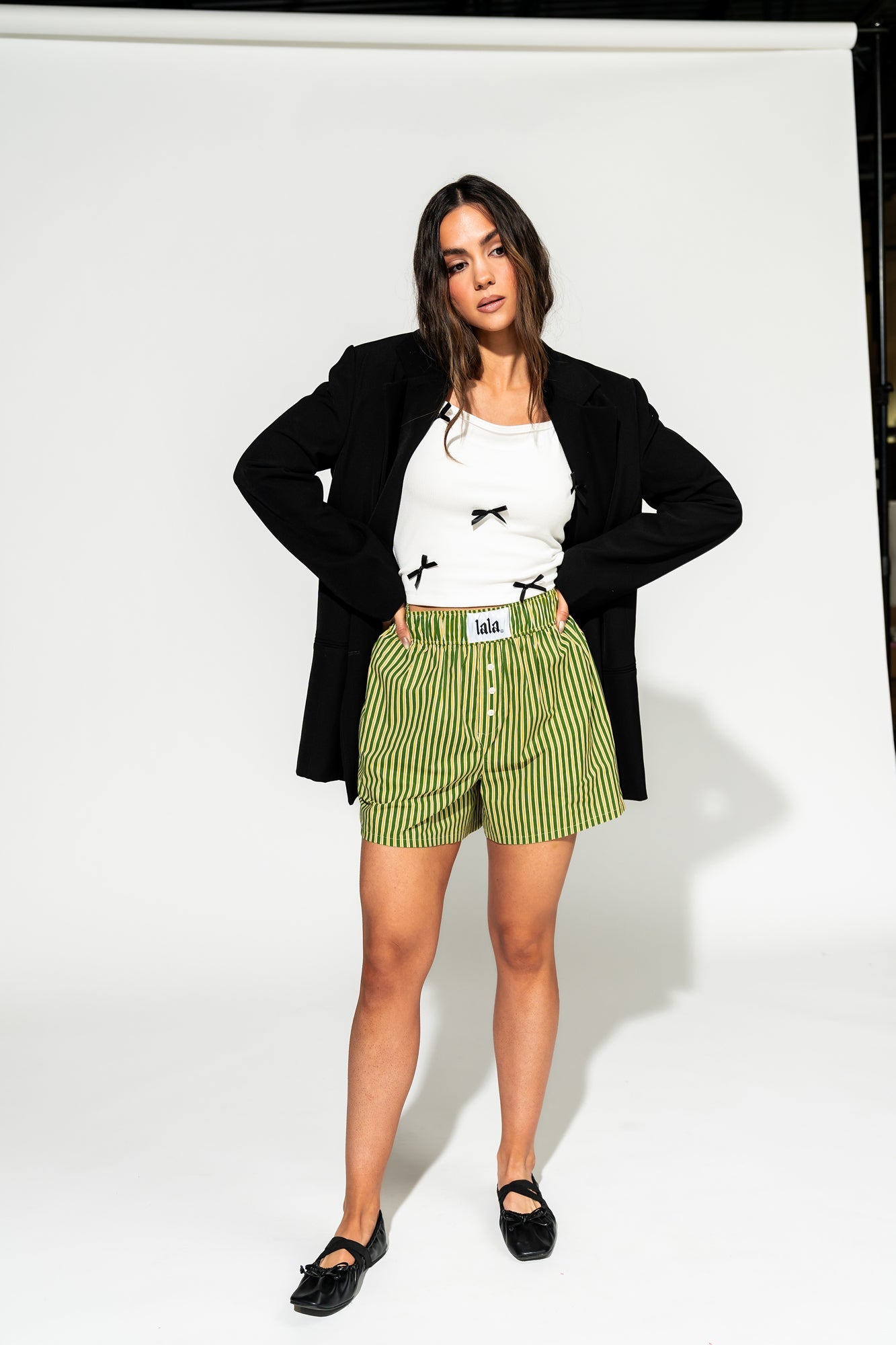 photo of girl wearing green and yellow stripe boxer shorts with elastic waistband that has a white "lala" label at the front, 3 button faux fly, and side pockets