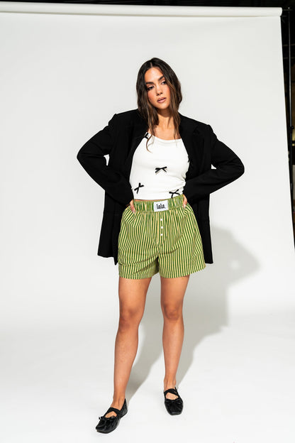 photo of girl wearing green and yellow stripe boxer shorts with elastic waistband that has a white "lala" label at the front, 3 button faux fly, and side pockets