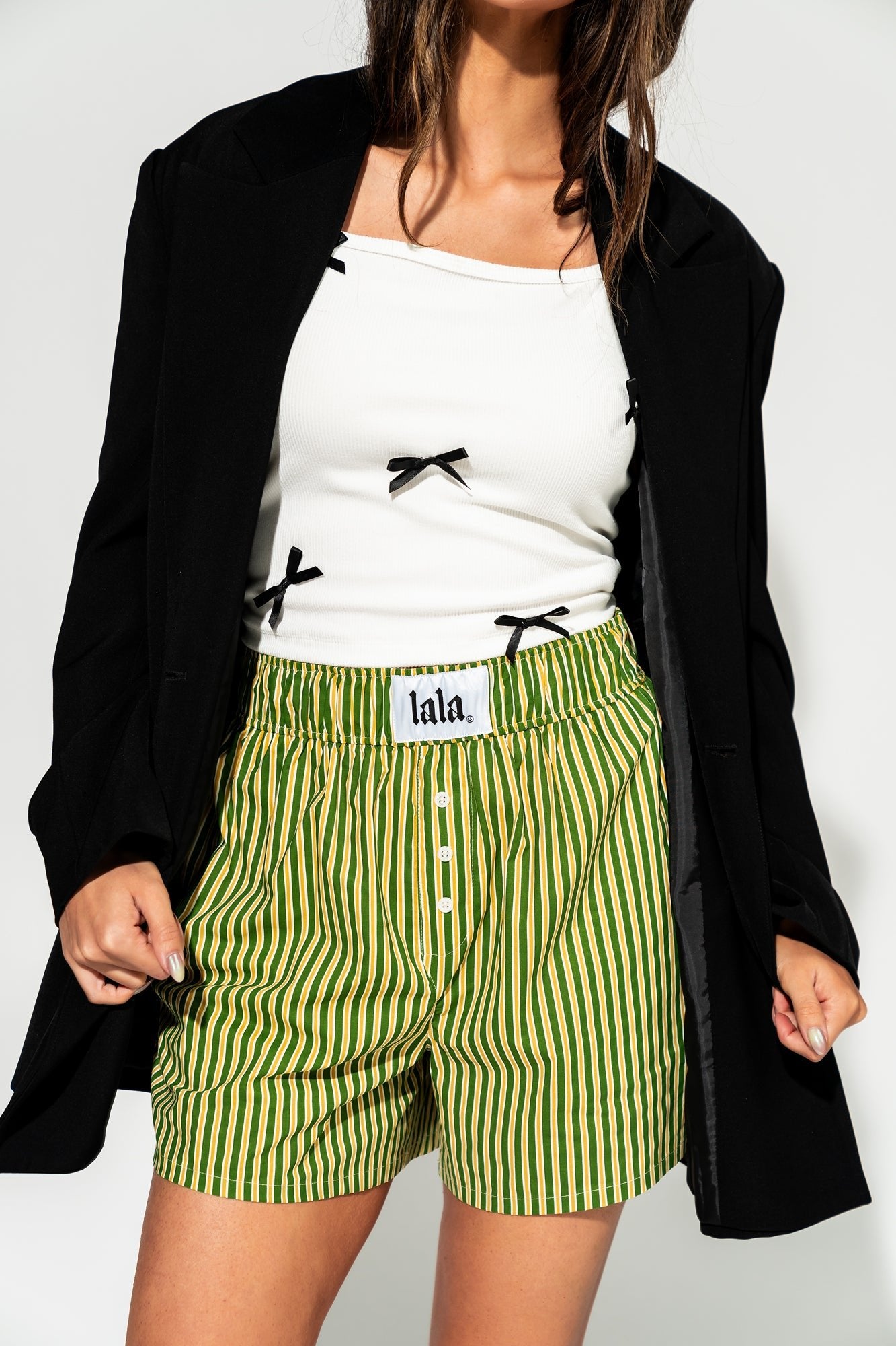 photo of girl wearing green and yellow stripe boxer shorts with elastic waistband that has a white "lala" label at the front, 3 button faux fly, and side pockets