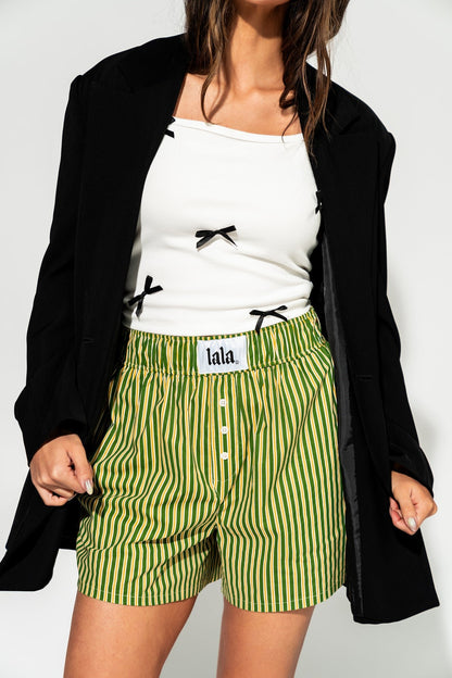 photo of girl wearing green and yellow stripe boxer shorts with elastic waistband that has a white "lala" label at the front, 3 button faux fly, and side pockets