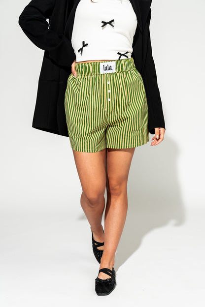 photo of girl wearing green and yellow stripe boxer shorts with elastic waistband that has a white "lala" label at the front, 3 button faux fly, and side pockets