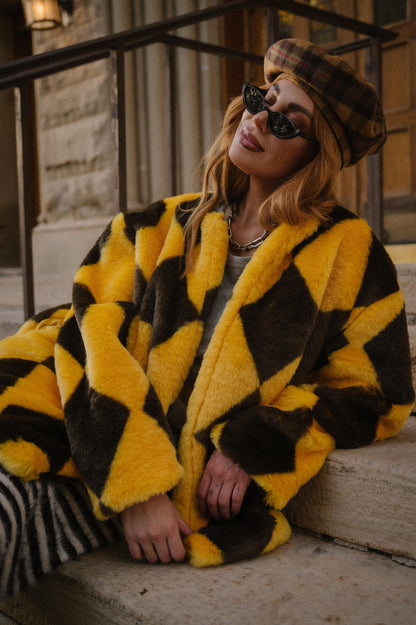 Person wearing a yellow and brown diamond faux fur coat sitting on steps.