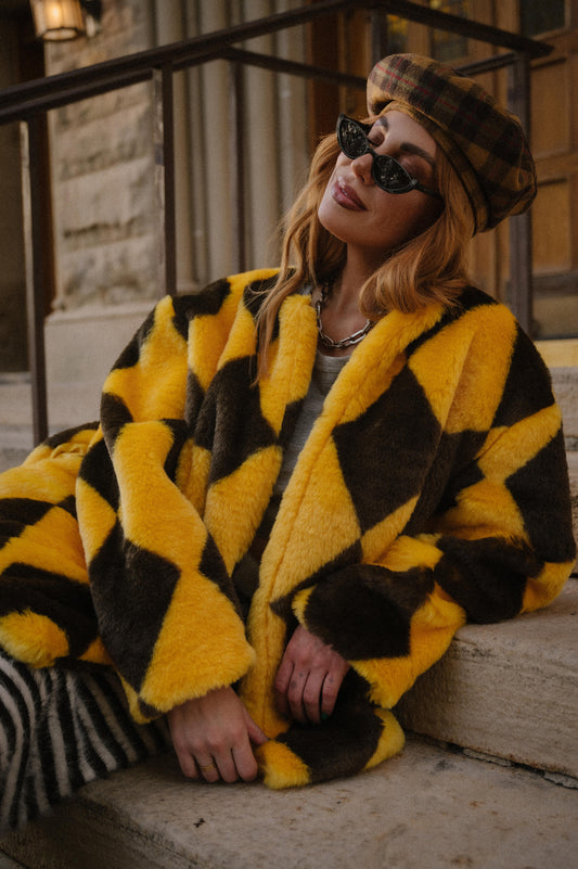 Person wearing a yellow and brown diamond faux fur coat sitting on steps.