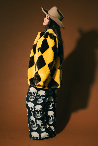 Person wearing a yellow and brown diamond faux fur coat with a beige cowboy hat on a brown background