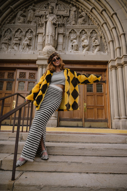 Person posing on steps in front of a decorative building entrance wearing a yellow and brown diamond faux fur coat.