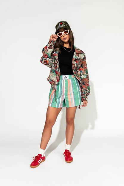 photo of girl wearing multi color stripe boxer shorts with elastic waistband with white label that says "lala" in the front, 3 button faux fly, and side pockets