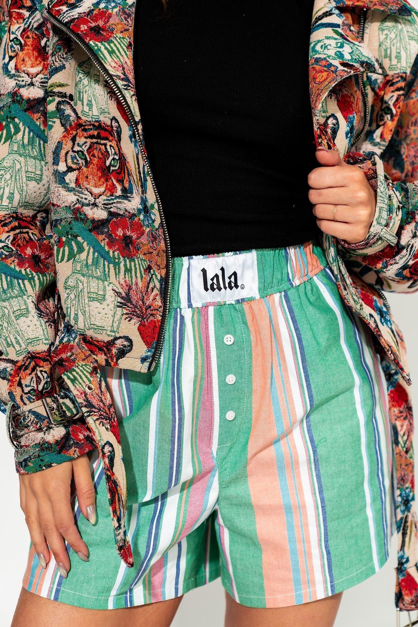 photo of girl wearing multi color stripe boxer shorts with elastic waistband with white label that says "lala" in the front, 3 button faux fly, and side pockets
