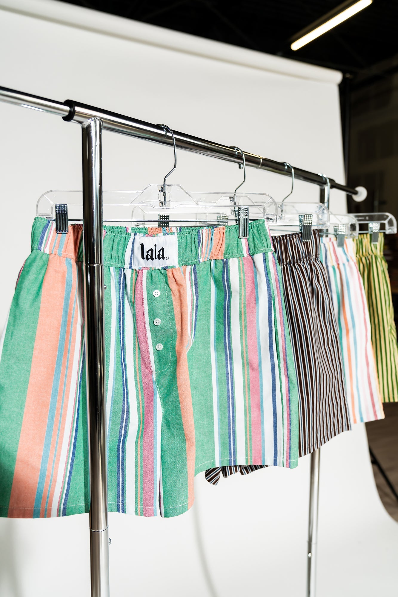 photo of girl wearing multi color stripe boxer shorts with elastic waistband with white label that says "lala" in the front, 3 button faux fly, and side pockets