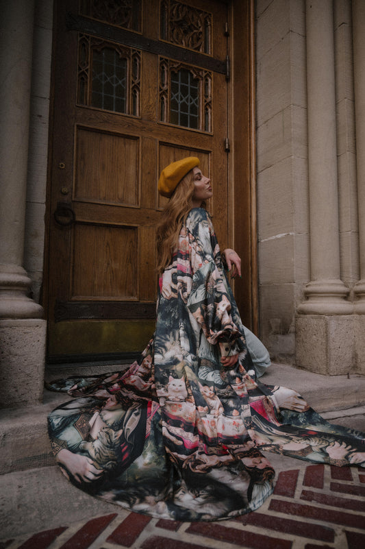 Woman in a satin duster with kitty pattern sitting on steps in front of a large wooden door.