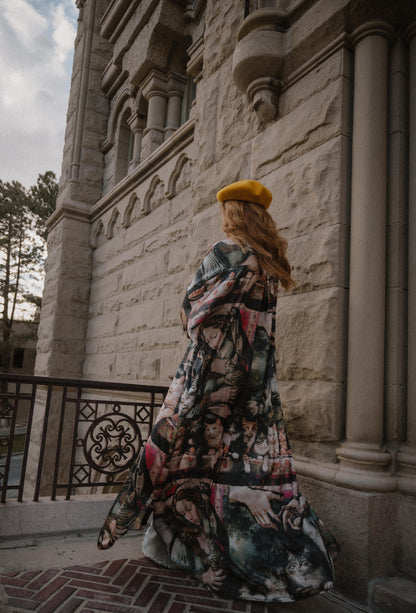Woman in a renaissance cat pattern satin duster and yellow beret standing in front of a stone building.