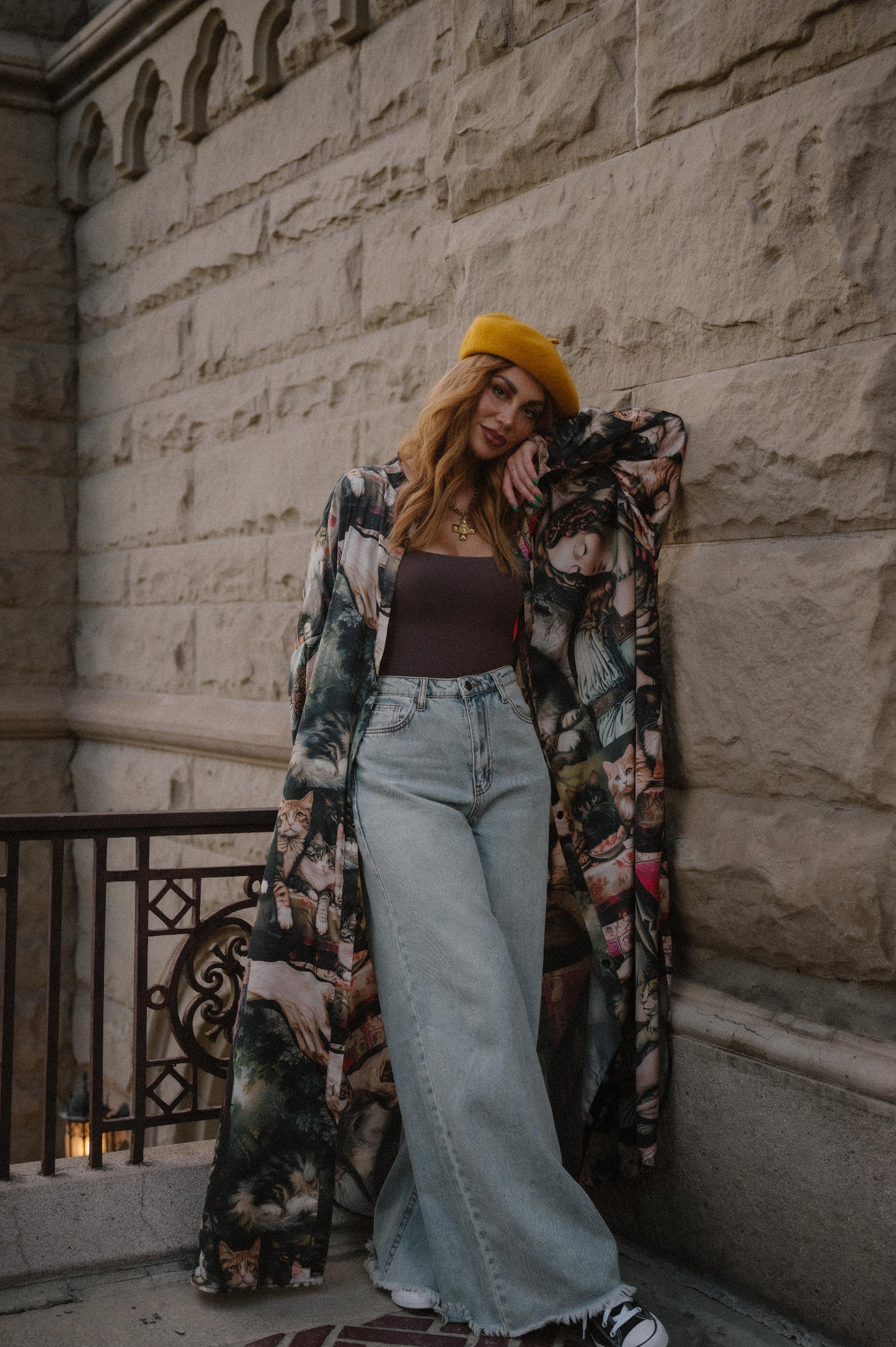 Woman wearing a renaissance cat satin duster and jeans standing against a stone wall.