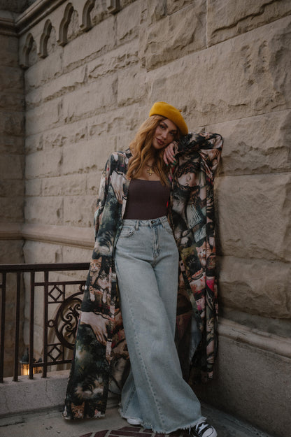 Woman wearing a renaissance cat satin duster and jeans standing against a stone wall.