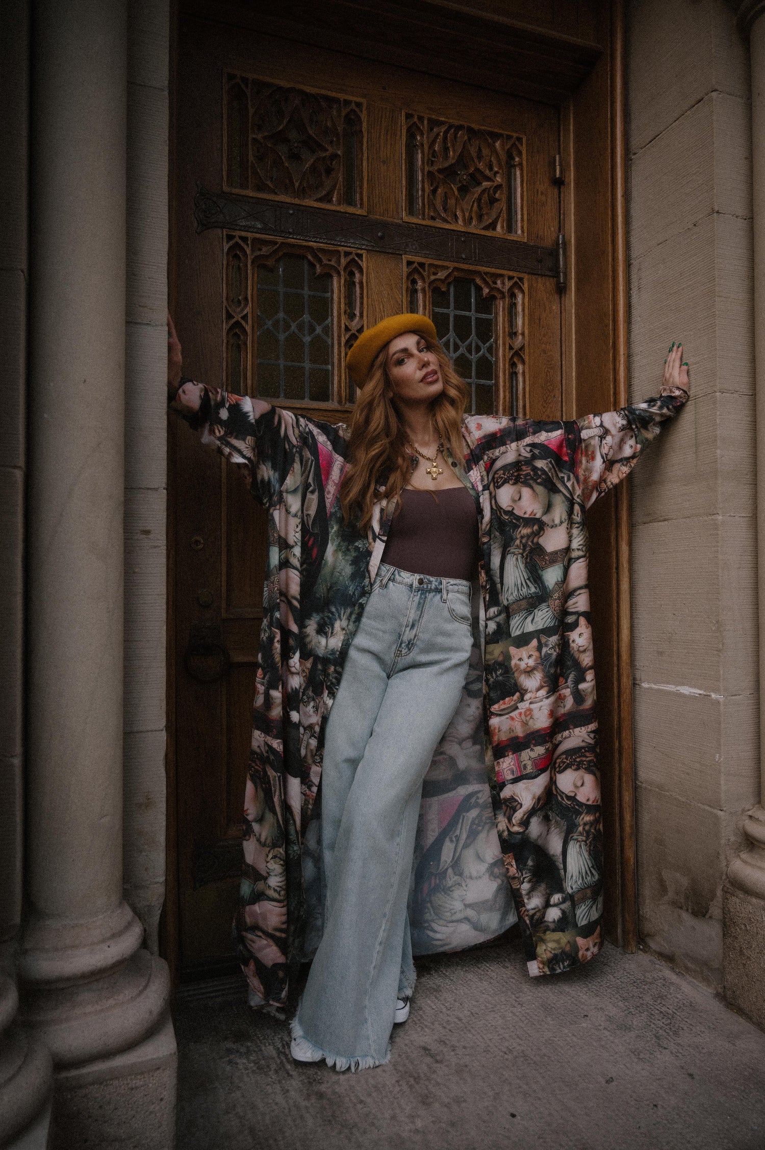 Woman in a renaissance cat satin duster and jeans standing in front of a wooden door.