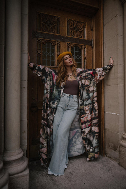 Woman in a renaissance cat satin duster and jeans standing in front of a wooden door.