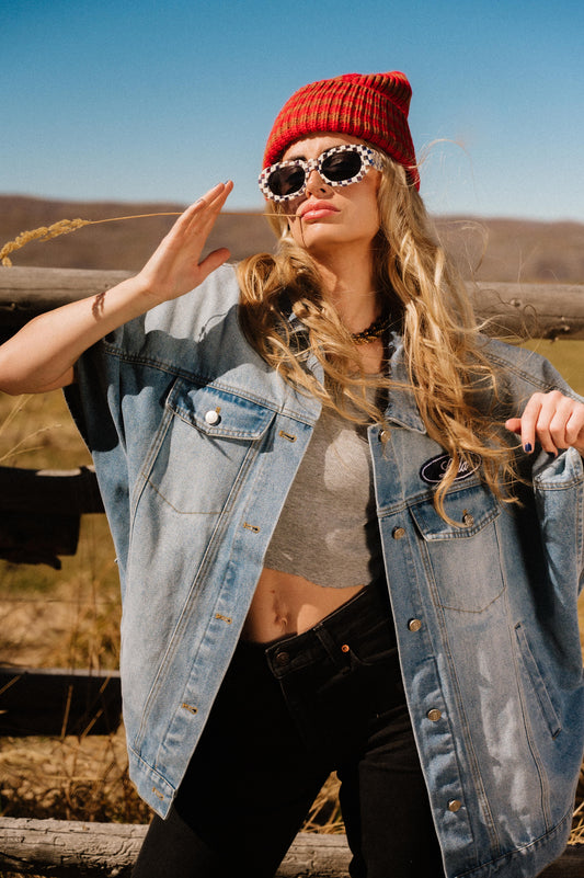 Woman wearing a red beanie, sunglasses, and denim jacket outdoors.