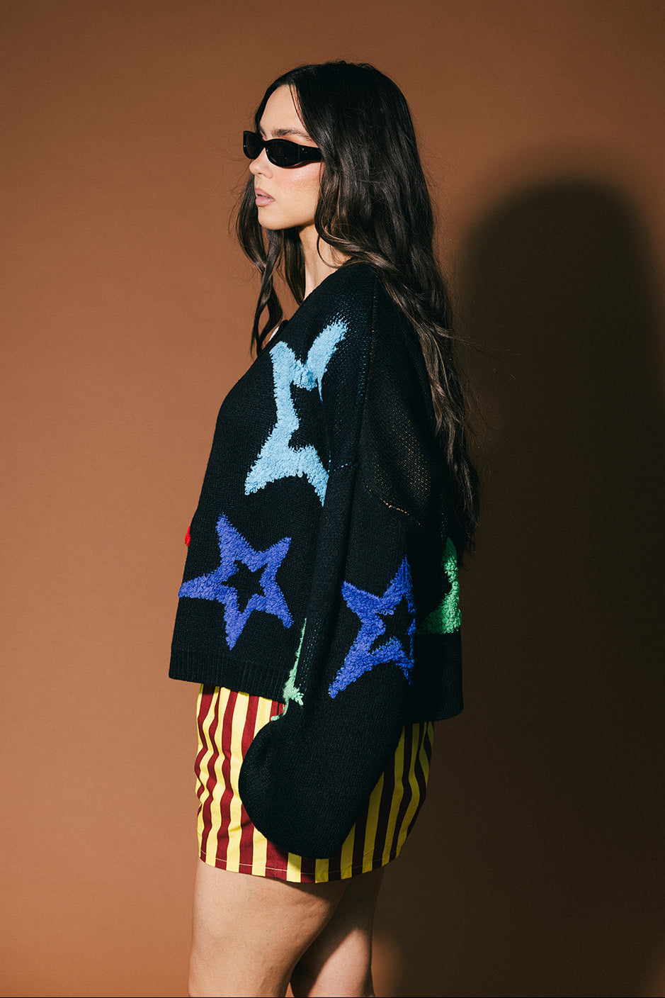 Woman wearing a black cardigan with colorful star patterns against a brown background