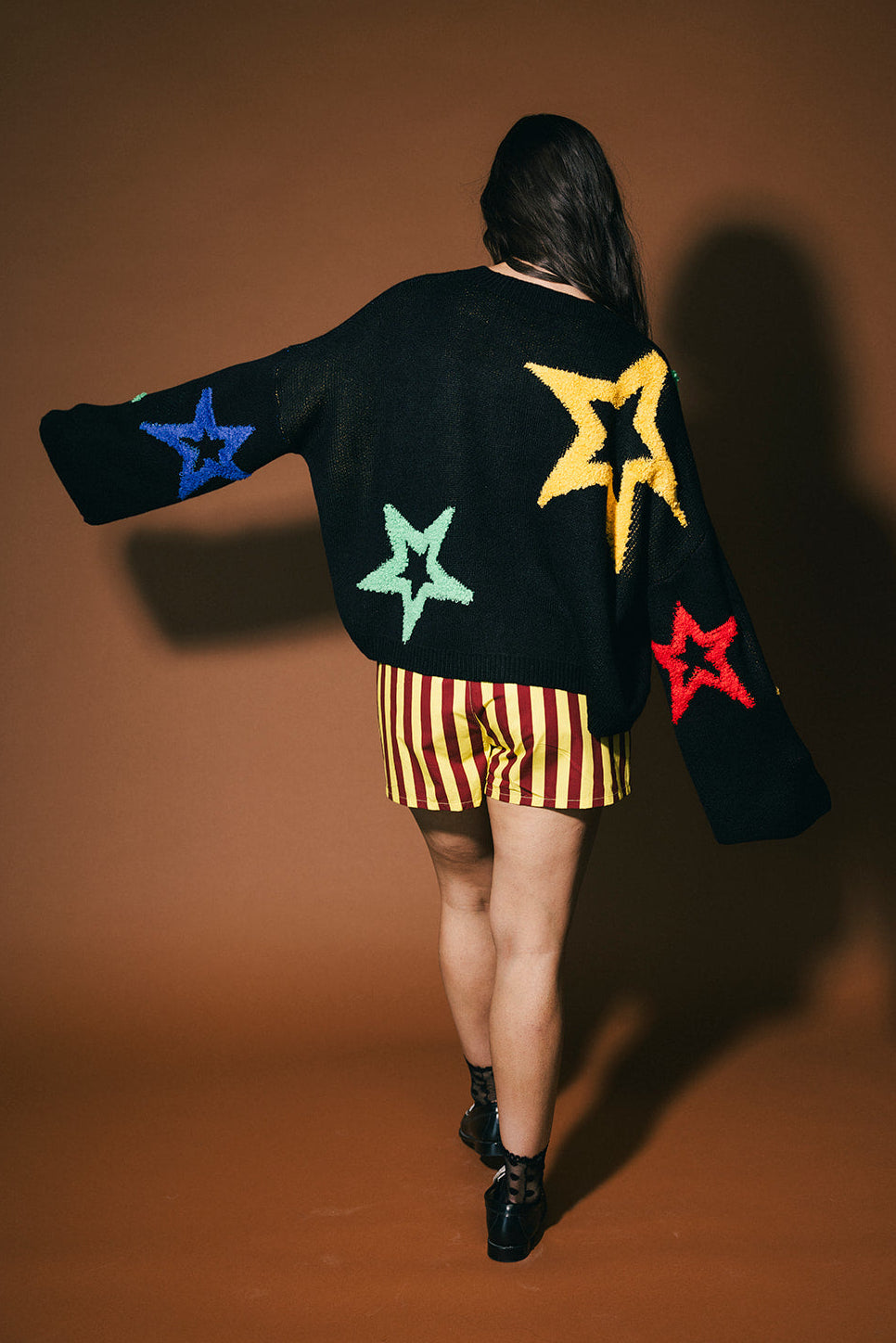 Person wearing a black sweater with colorful star patterns on a brown background