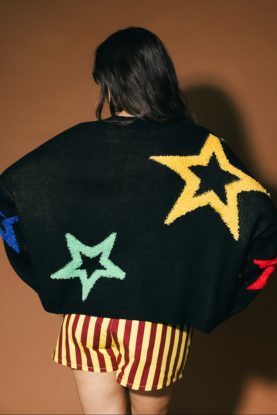 Person wearing a black sweater with colorful star designs on a brown background