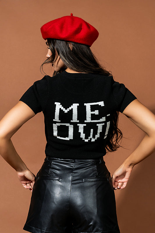 Person wearing a black t-shirt with 'MEOW' printed on it, red beret, and black leather skirt against a brown background