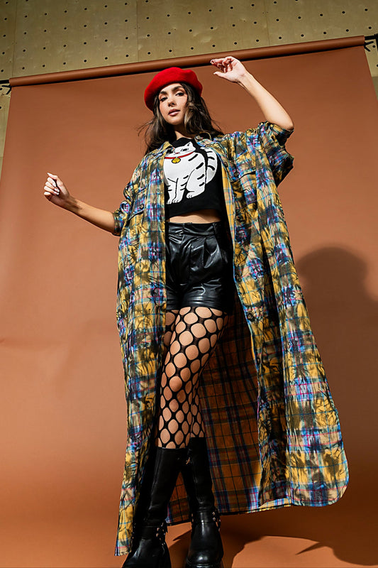 Woman wearing a colorful coat, black top, and leather shorts against a brown backdrop