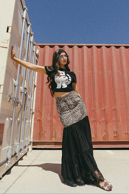 Woman standing in front of shipping containers wearing a black t-shirt with a graphic design and a long black skirt.