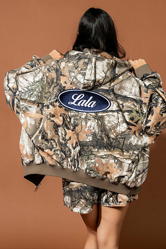 Person wearing a camouflage jacket with 'Lala' logo on a brown background