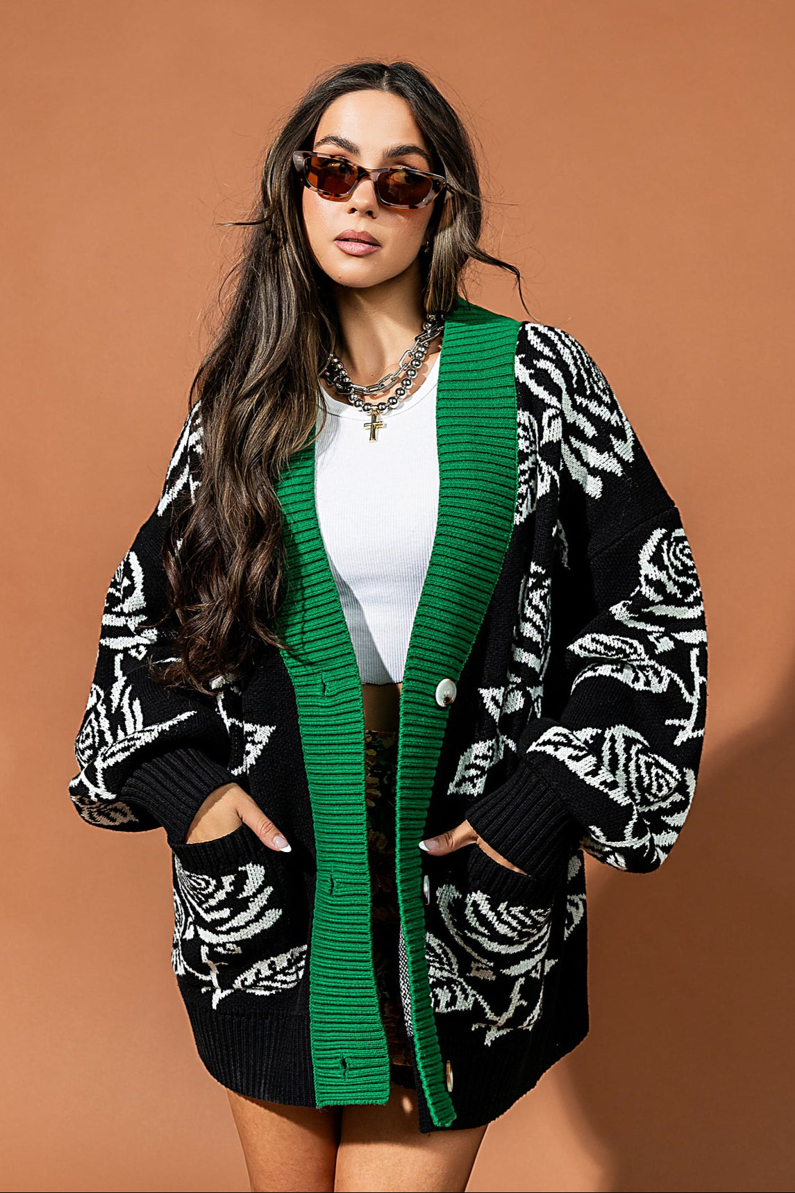 Woman wearing a black and white patterned cardigan with green trim against a brown background