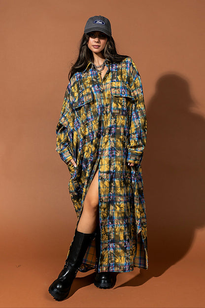 Woman wearing a plaid dress with a high slit, black boots, and a cap on a brown background