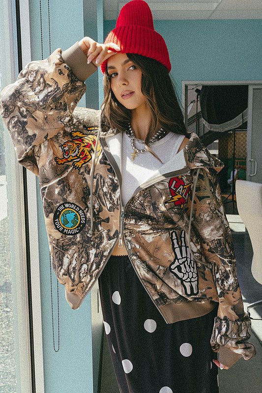 Person wearing a camouflage jacket with patches, a red beanie, and polka dot pants indoors.