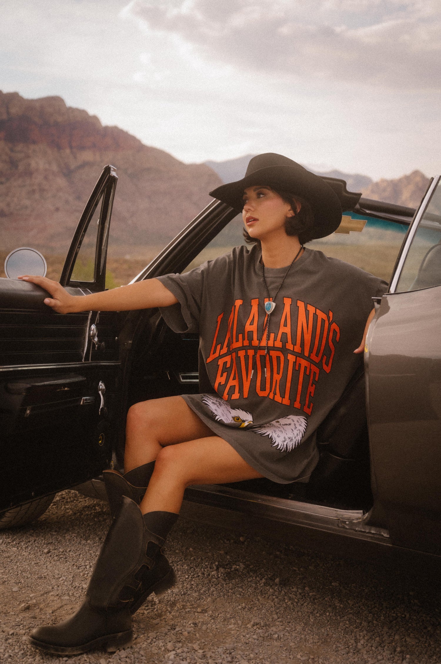 Person wearing a shirt with 'Lalaland's Favorite' text, sitting in an open car door outdoors.