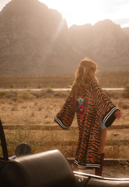 Person wearing a tiger-striped robe with a colorful design, standing in a desert-like landscape.