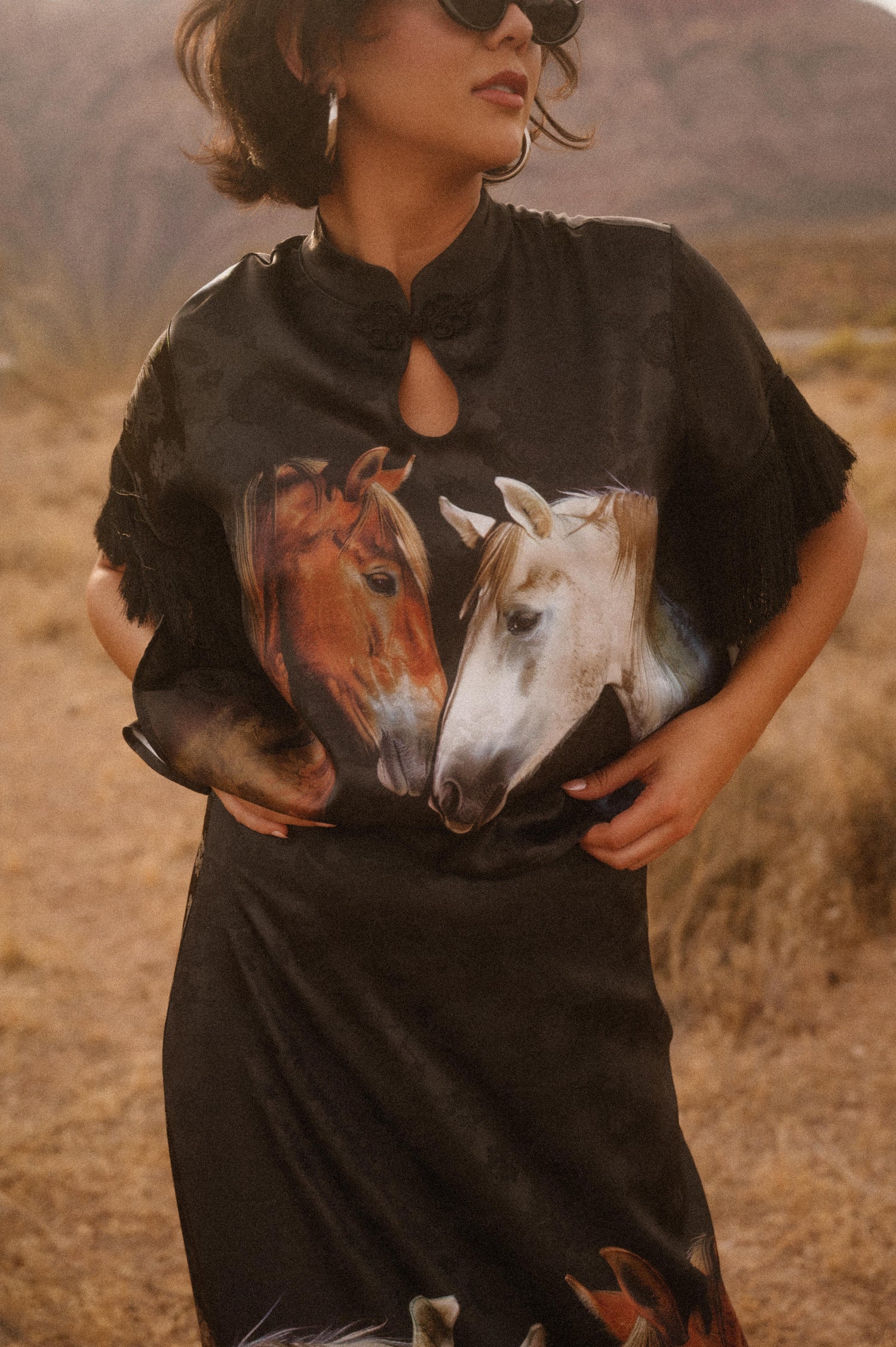 Woman wearing a black poncho with horse design in a desert setting