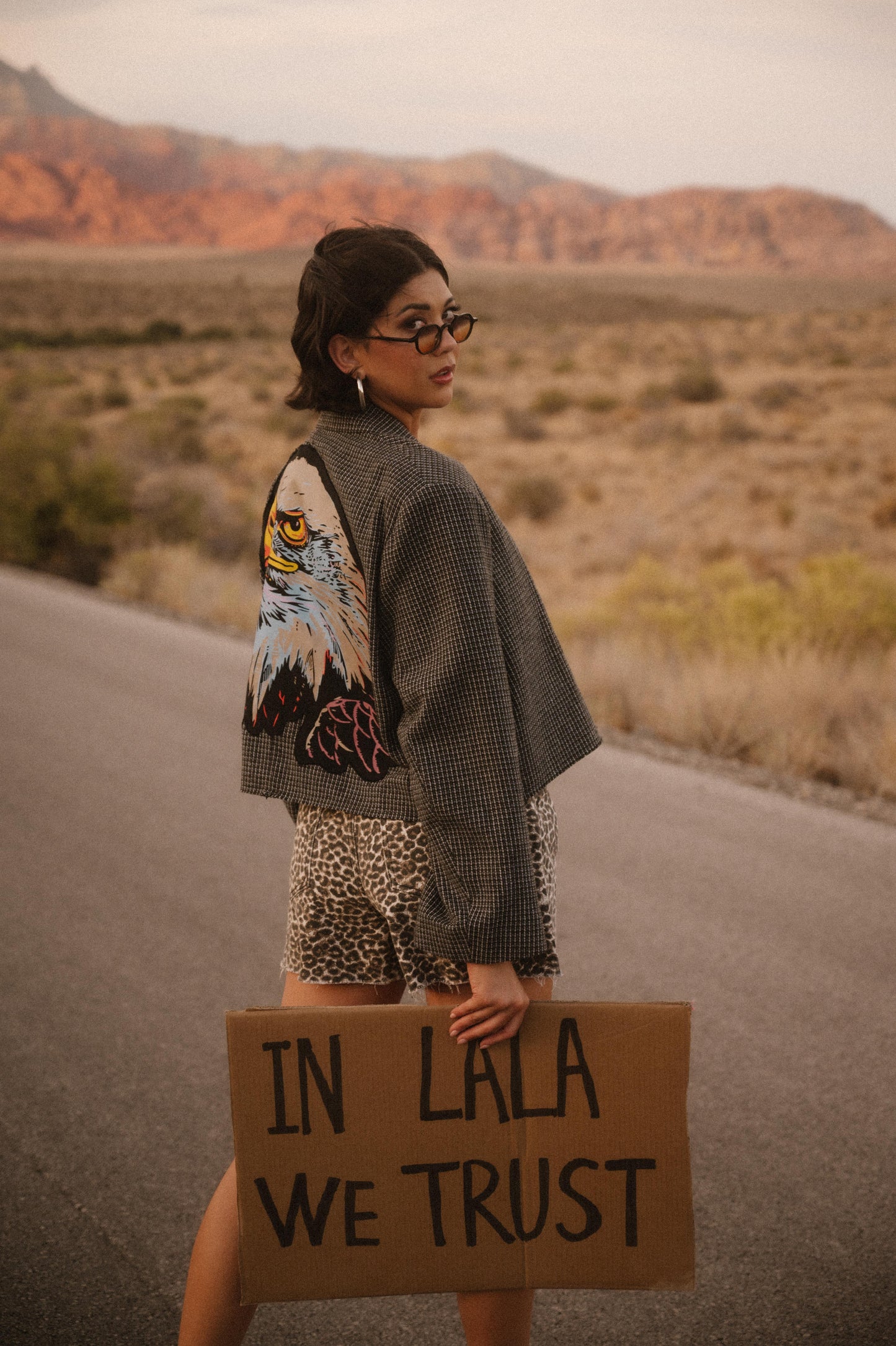 Person holding a sign with 'IN LALA WE TRUST' in a desert setting