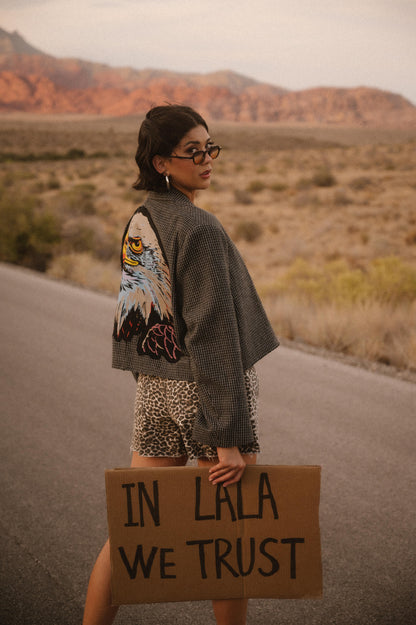 Person holding a sign with 'IN LALA WE TRUST' in a desert setting
