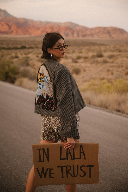 Person holding a sign with 'IN LALA WE TRUST' in a desert setting