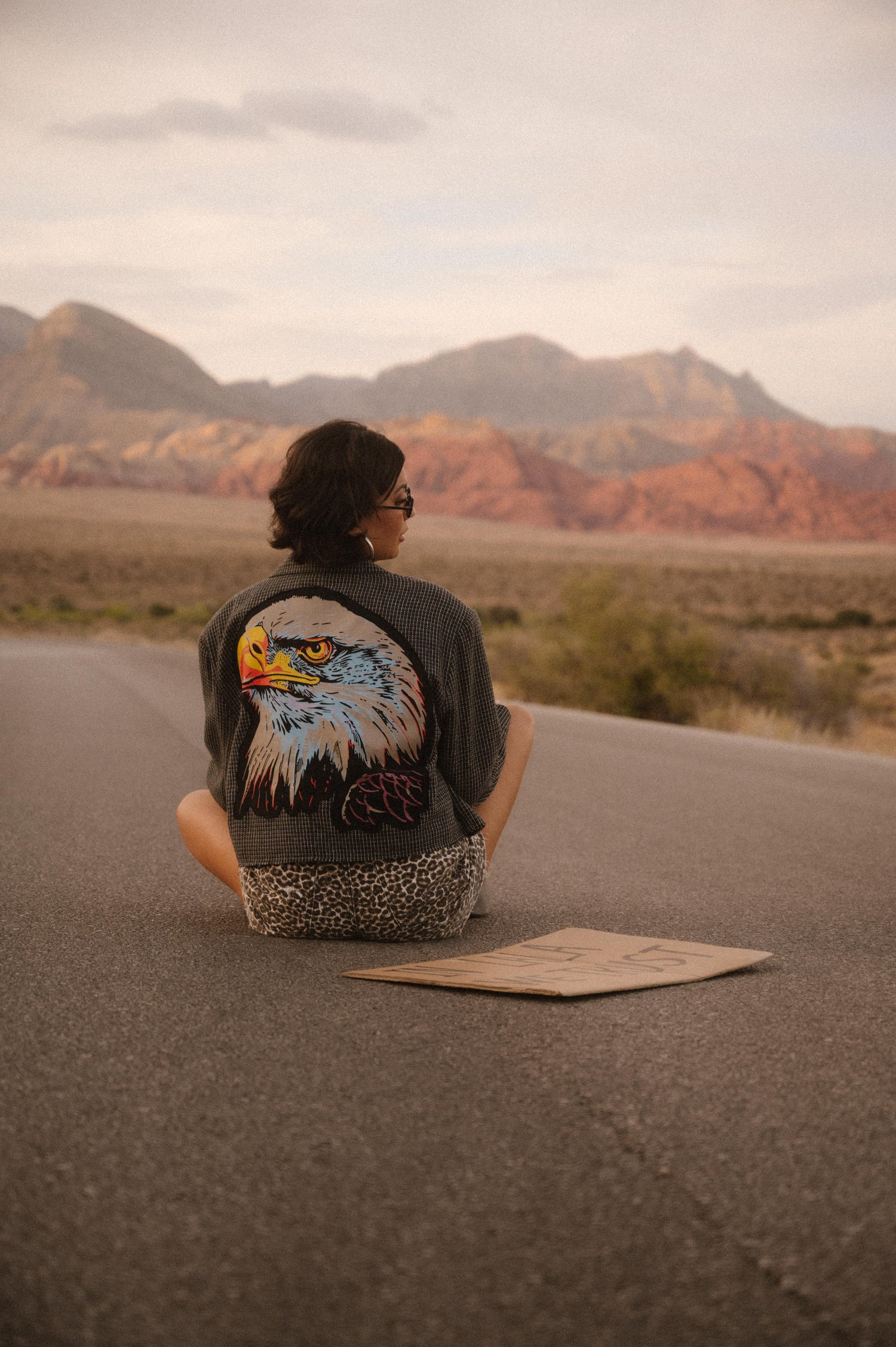 Person sitting on a road with a scenic desert landscape and mountains in the background