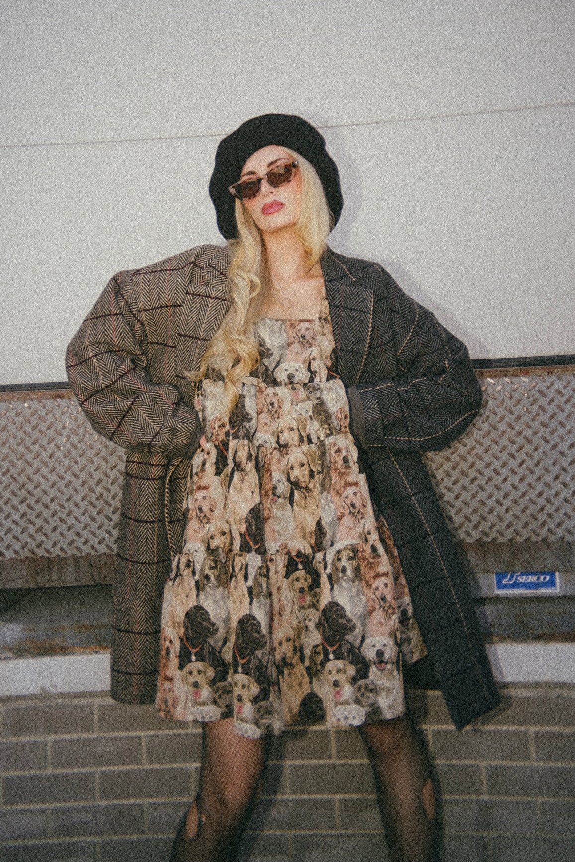 Person wearing a patterned dress and coat against a plain wall.