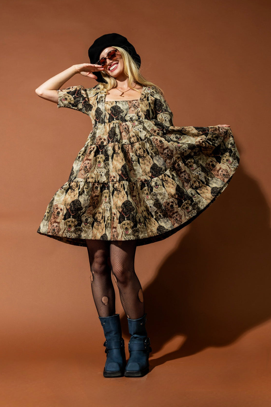 Woman in a floral dress and blue boots posing against a brown background