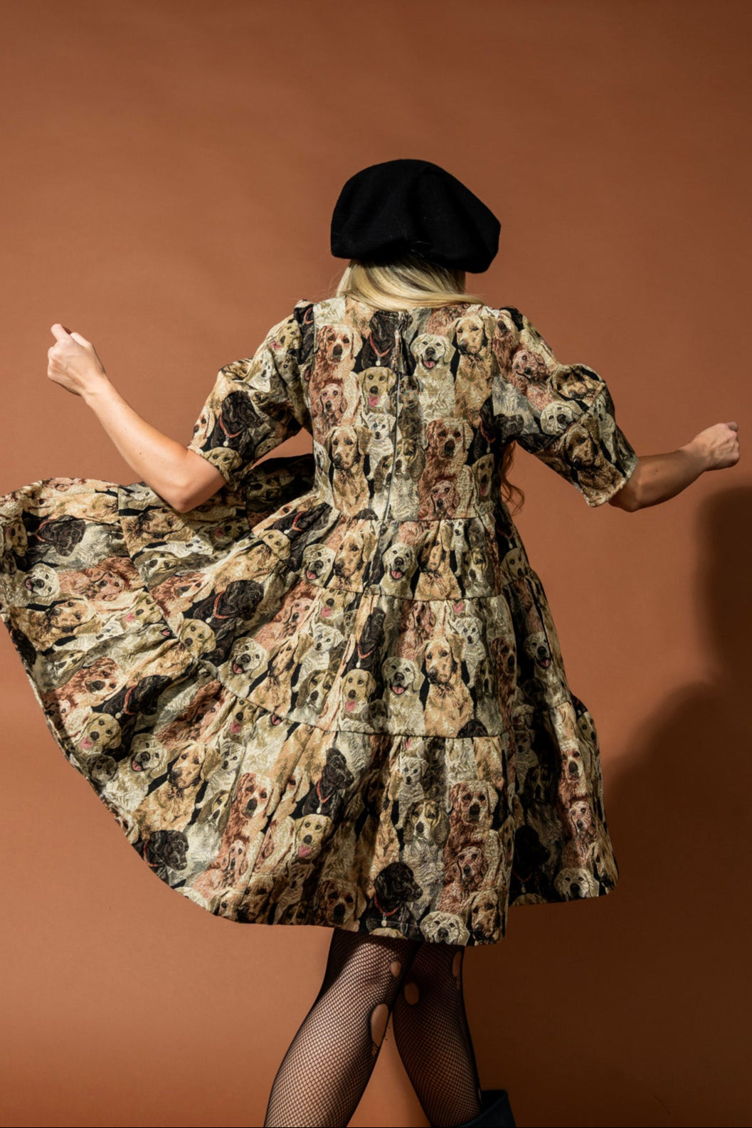 Woman in a dog patterned dress and black beret twirling against a brown background