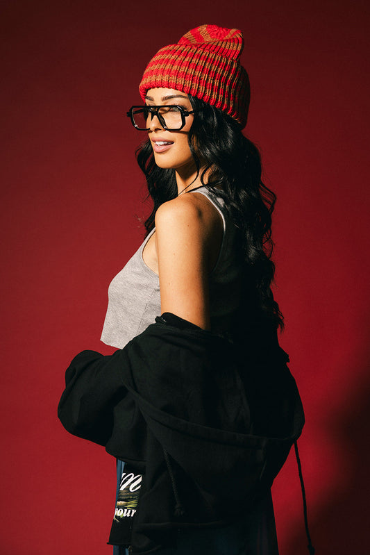 Woman wearing a red beanie and glasses against a red background