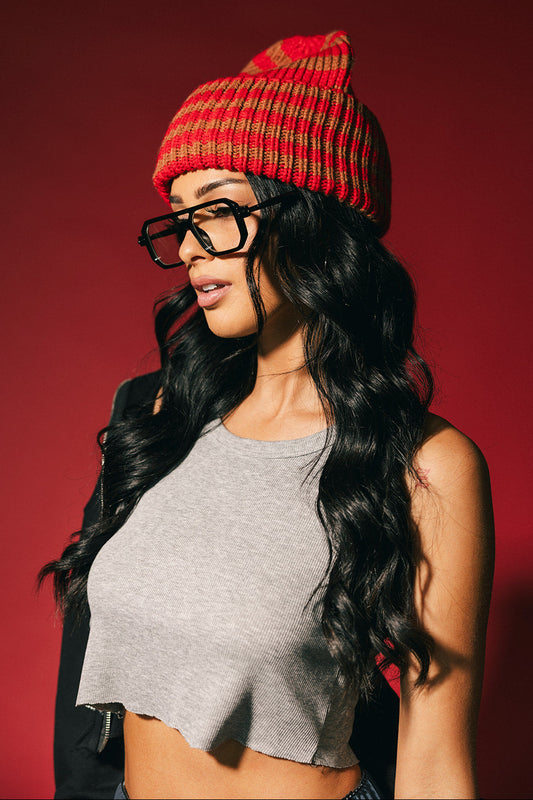 Woman wearing a red striped beanie and black glasses against a red background