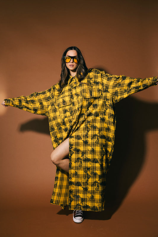 Person wearing a yellow and black plaid dress against a brown background