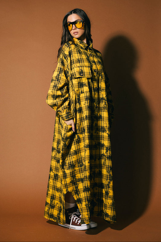 Person wearing a yellow and black plaid dress against a brown background