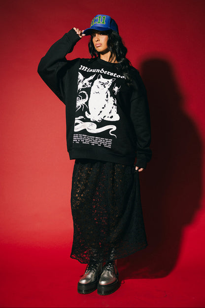 Person wearing a black sweatshirt with a graphic design, black pants, and a blue cap on a red background