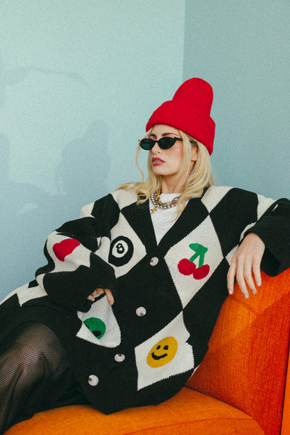 Person wearing a colorful cardigan with cartoon designs, sitting on an orange couch against a light blue wall.