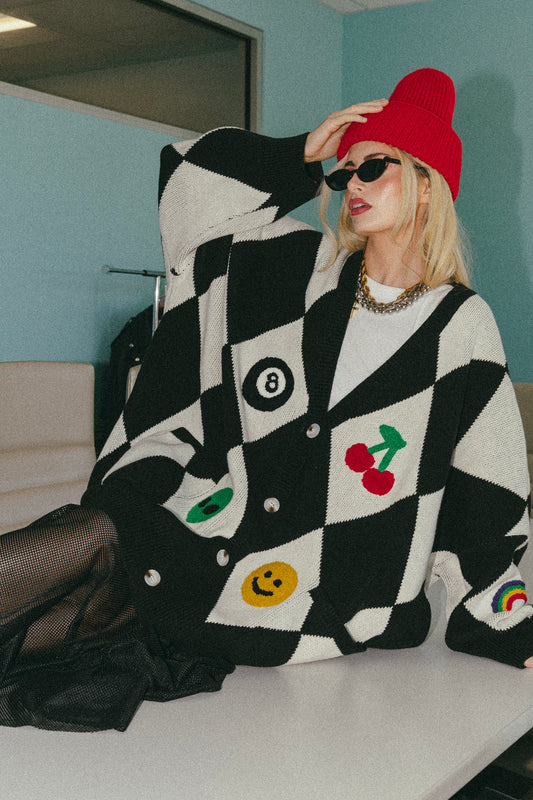Person wearing a black and white checkered sweater with colorful designs, sitting on a table.